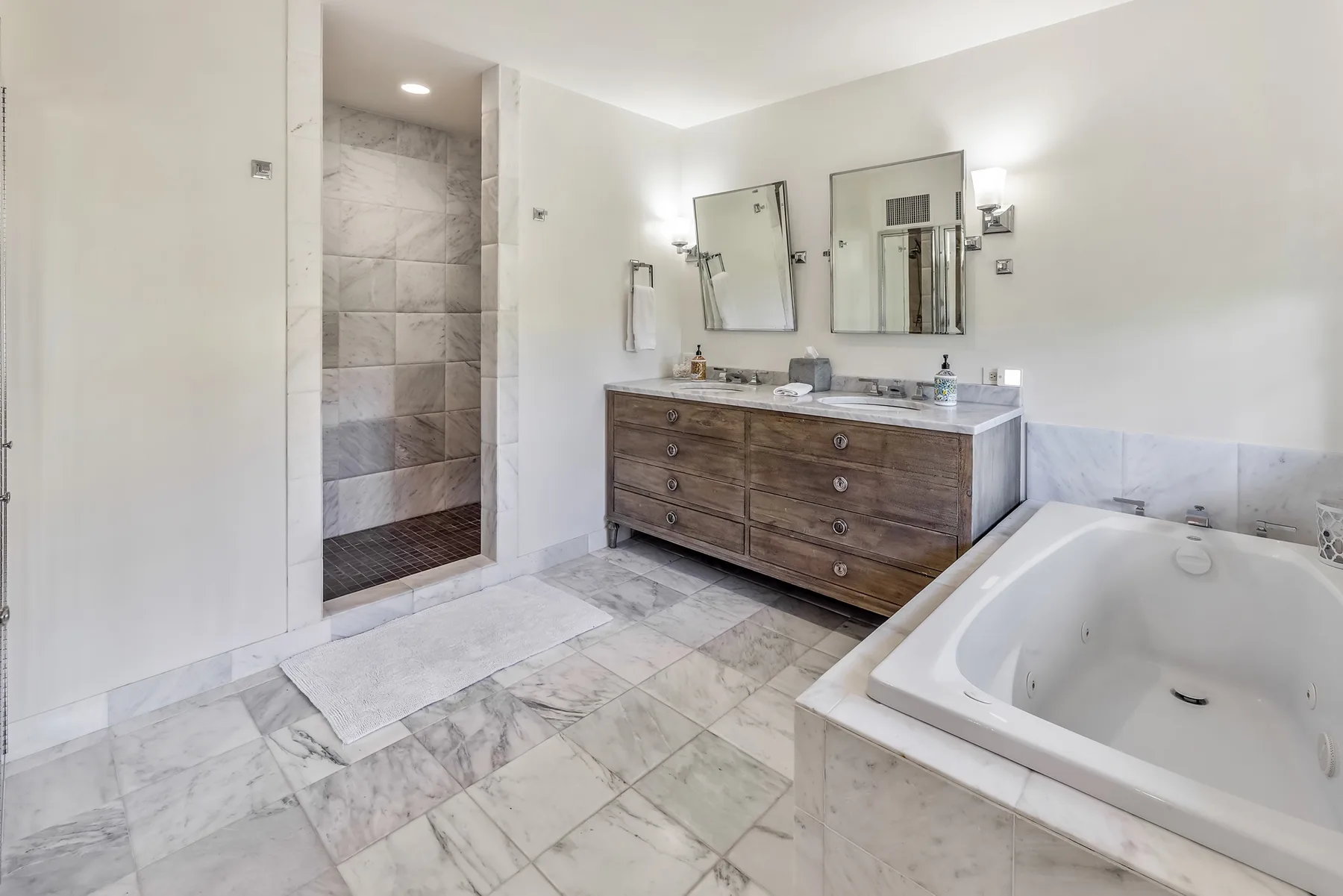 A bright bathroom with a double vanity, mirrors, and a bathtub.