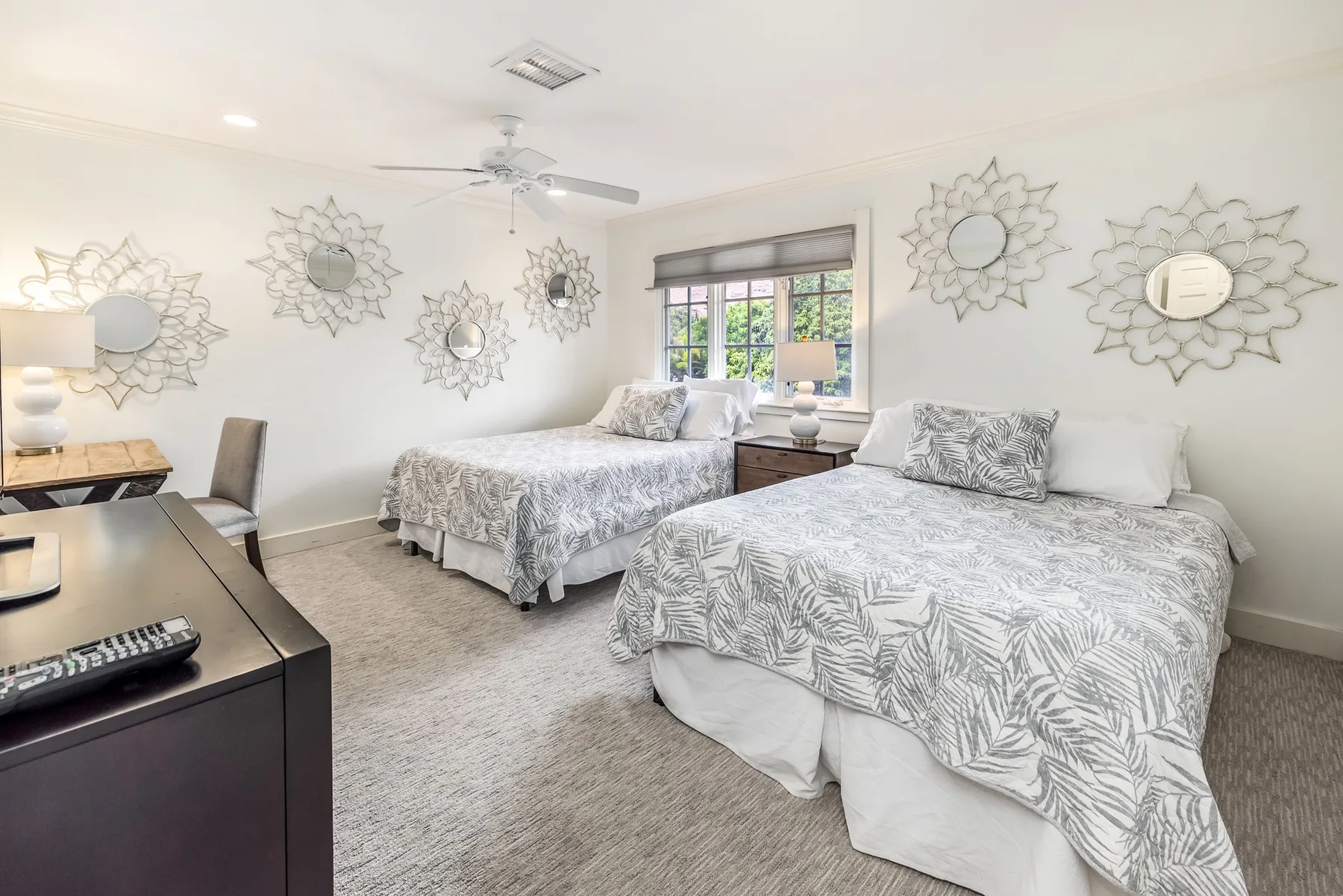 A bright bedroom with two beds and decorative mirrors on the walls.