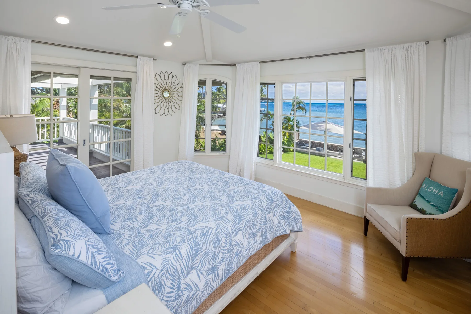 A bright bedroom with a bed beside large windows overlooking the ocean.