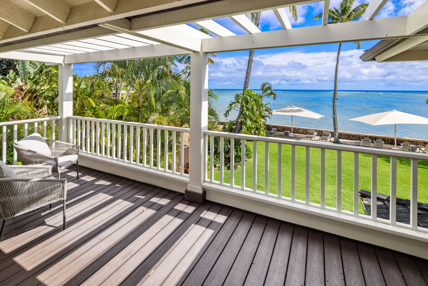 A covered outdoor deck overlooks a green lawn and the ocean.