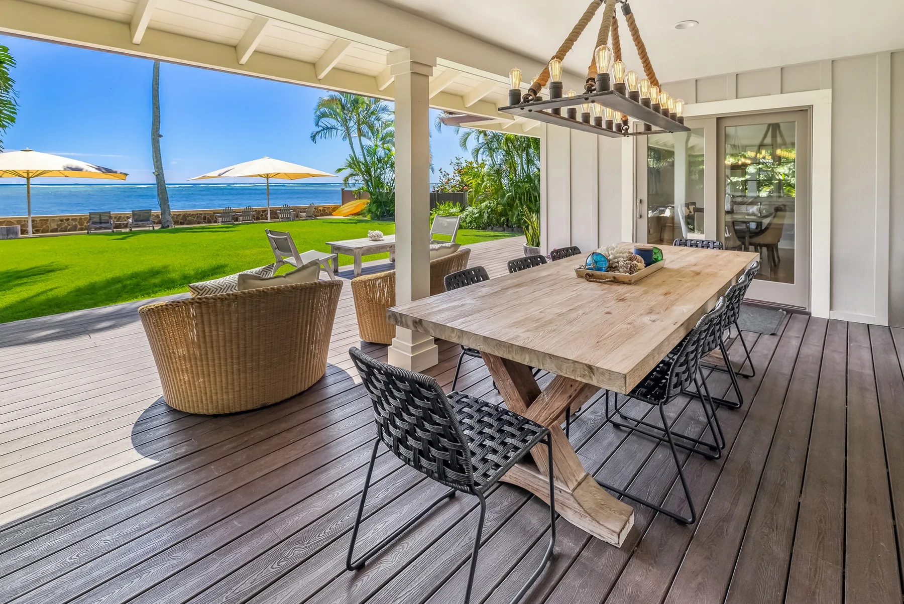 A covered outdoor dining area opens onto a lawn with a view of the water.