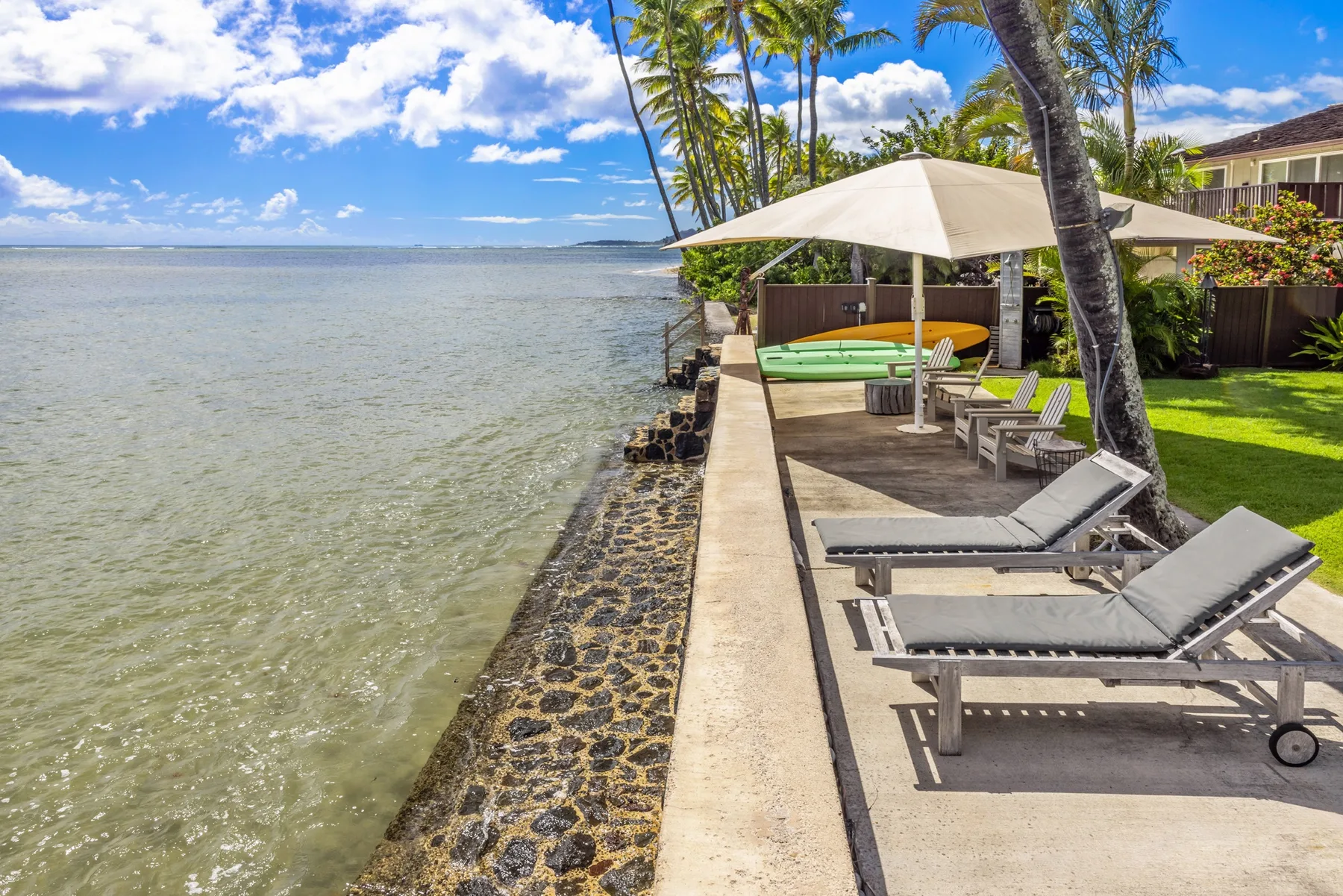 A waterfront patio with lounge seating and a large shade umbrella overlooks the water.
