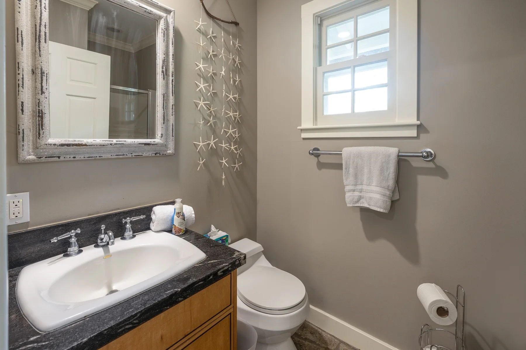 A bathroom with a sink, toilet, and towel hanging below a window.