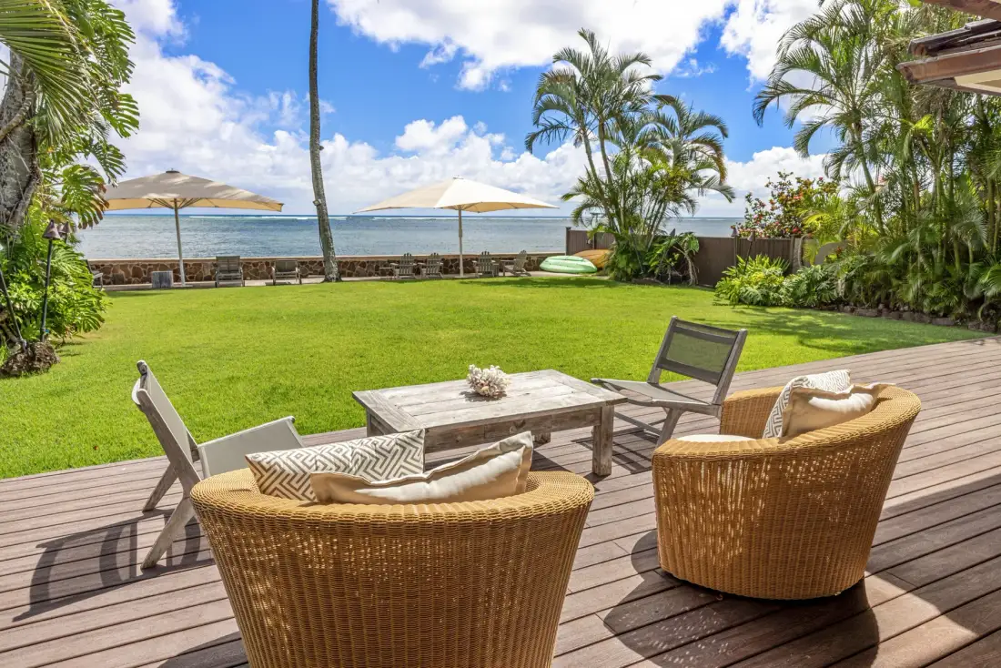 A seaside patio with outdoor seating overlooks a green lawn and the ocean.