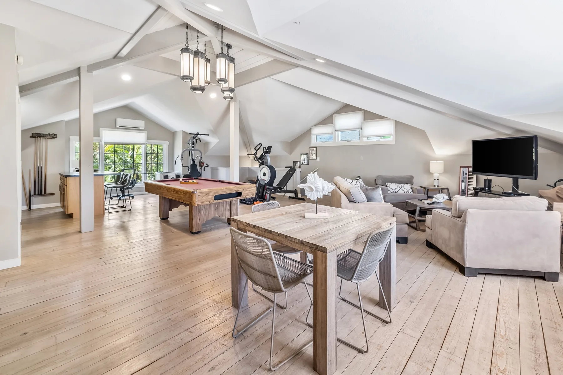 An open-plan living and recreation area with a dining table, seating, and exercise equipment.