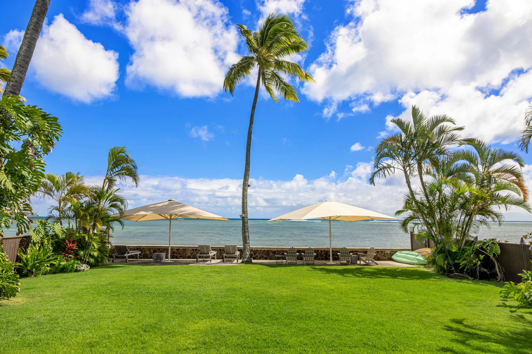 A seaside lawn with palm trees and umbrellas beside the water.