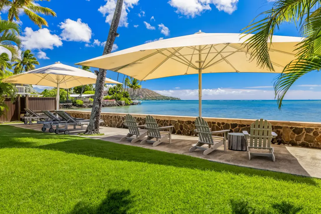 A grassy seaside patio with lounge seating and large shade umbrellas overlooks the ocean.