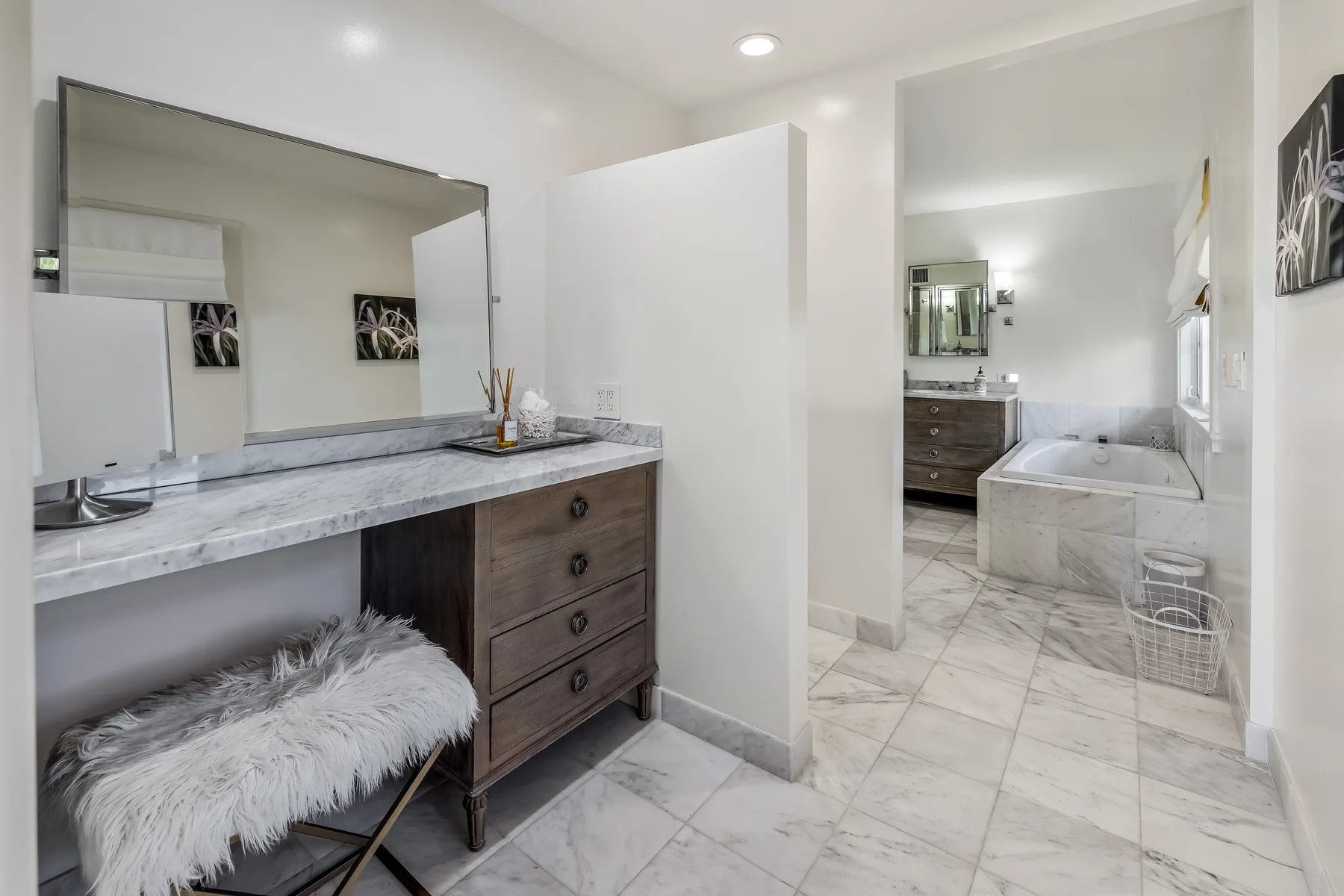 A bright bathroom with a long vanity and a bathtub in the adjoining area.