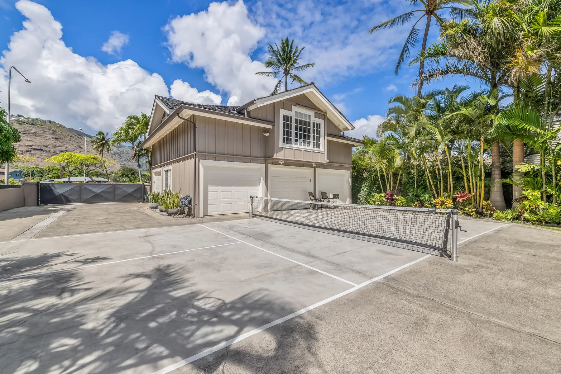 A building with garage doors faces a paved parking area bordered by tropical landscaping.
