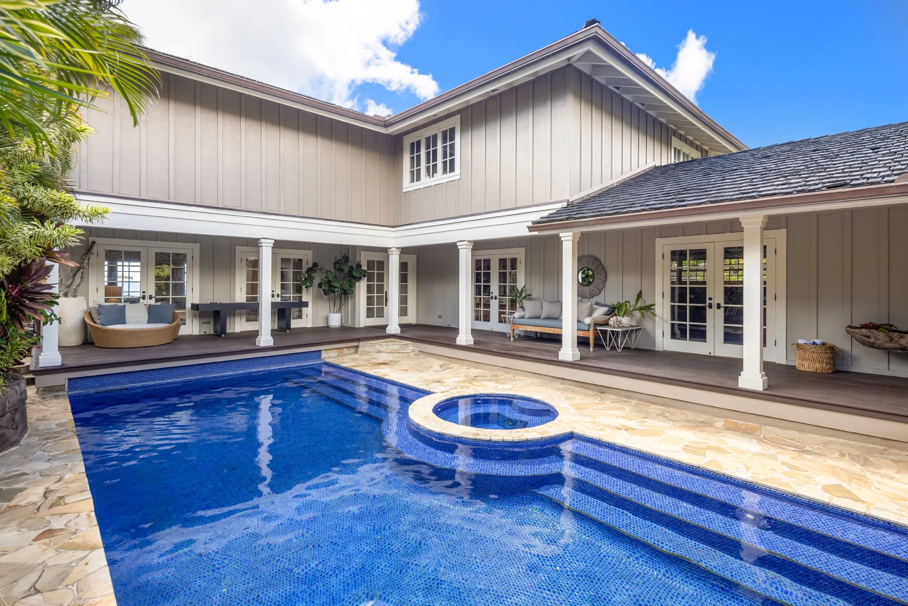 A blue swimming pool sits beside a covered patio with white columns.