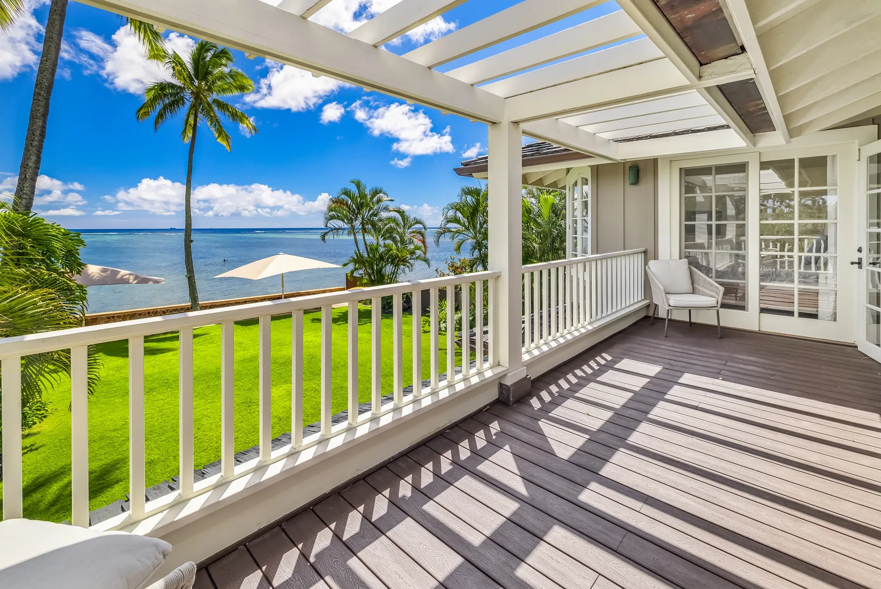 A covered deck overlooks a green lawn and ocean, with white railings.