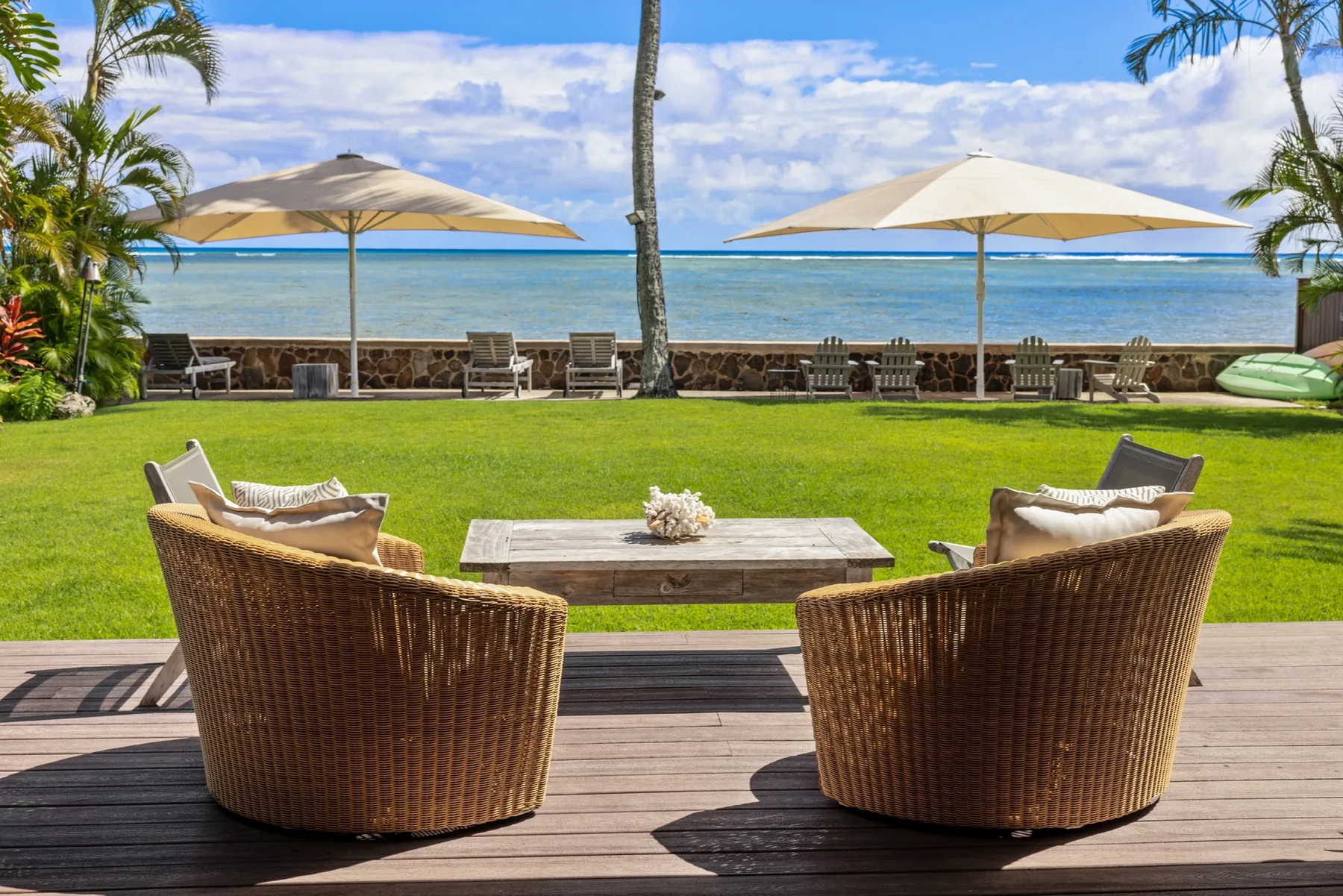 Outdoor patio seating overlooks a green lawn, beach, and ocean.