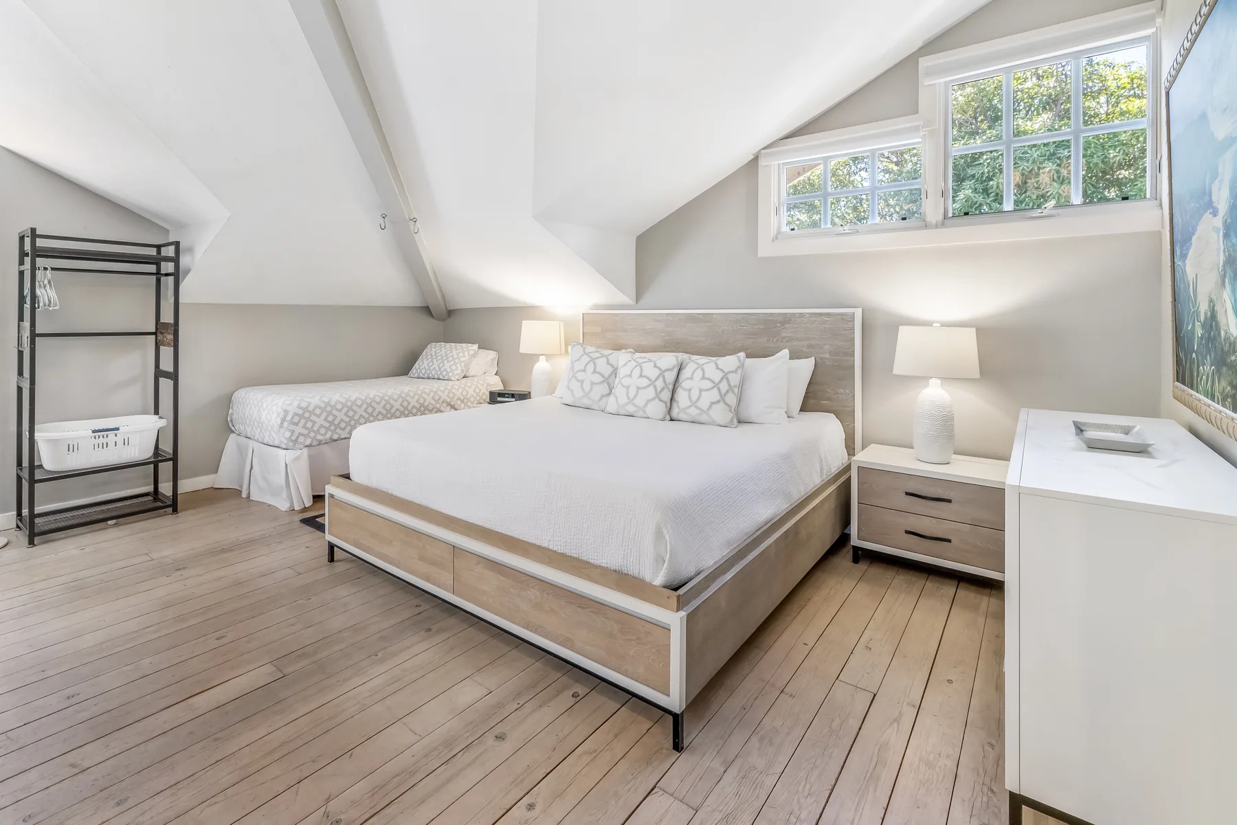 A bright bedroom with a large bed and a smaller bed beneath sloped ceilings.