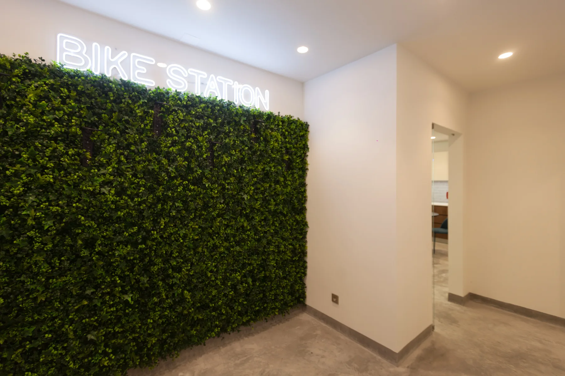 Un pasillo interior luminoso tiene una pared verde frondosa bajo un letrero iluminado.