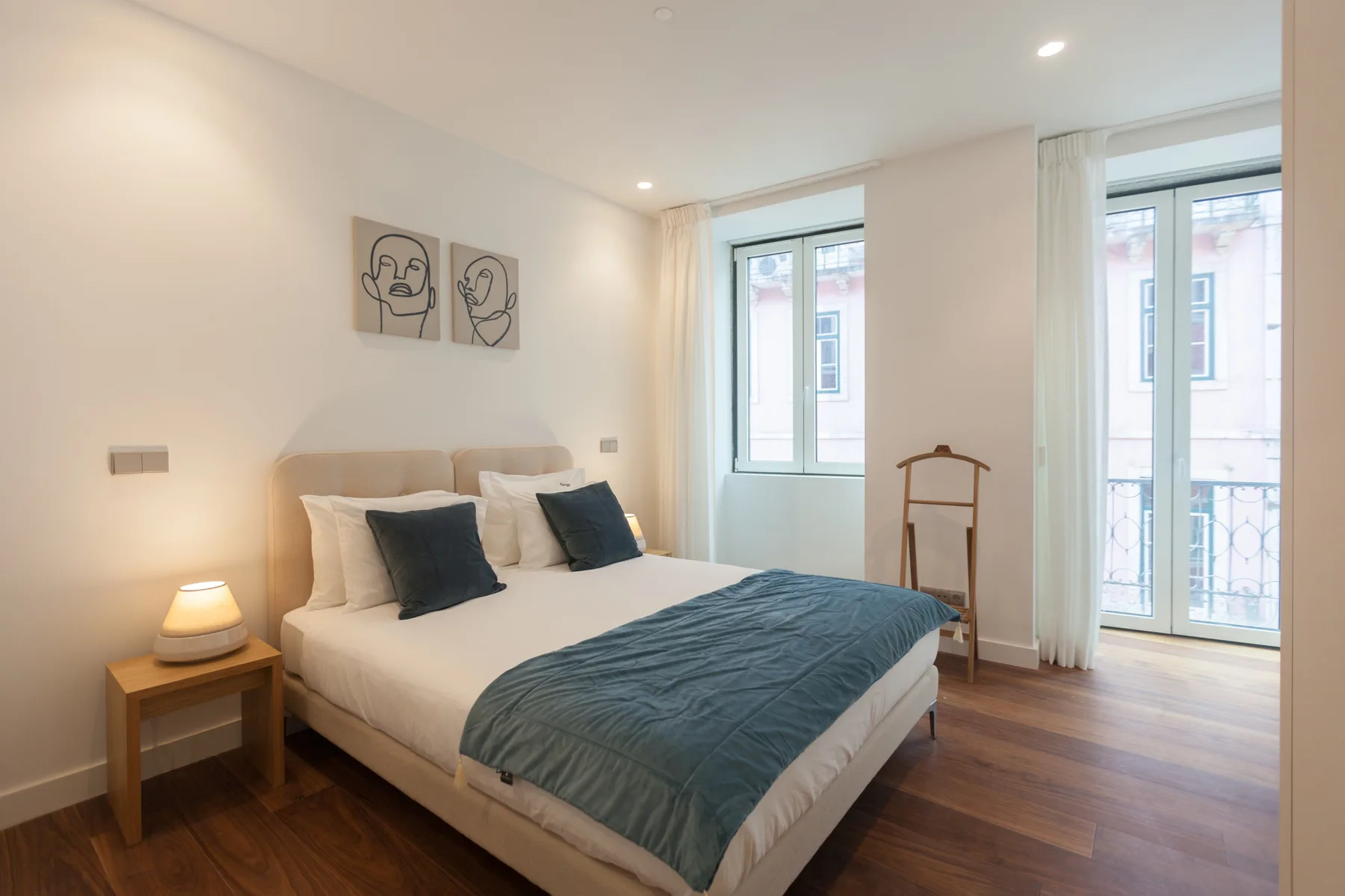 Un dormitorio con una cama, una mesita de noche y ventanas altas.
