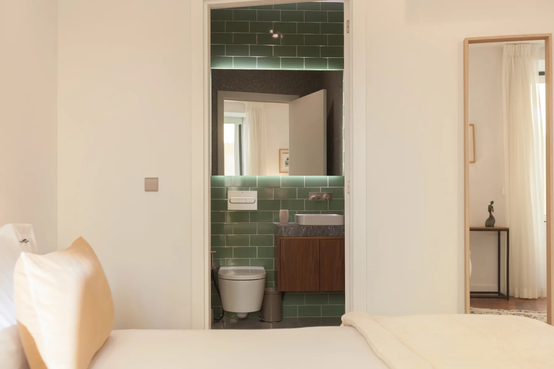 Un dormitorio da a un baño con paredes de azulejos verdes y un tocador.