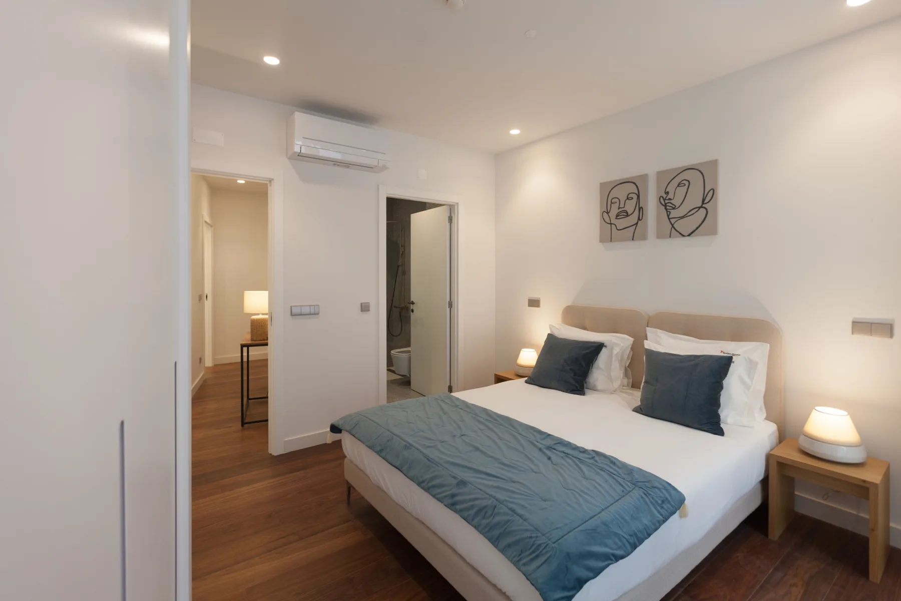 Un dormitorio con una cama tendida y cuadros enmarcados sobre el cabecero.