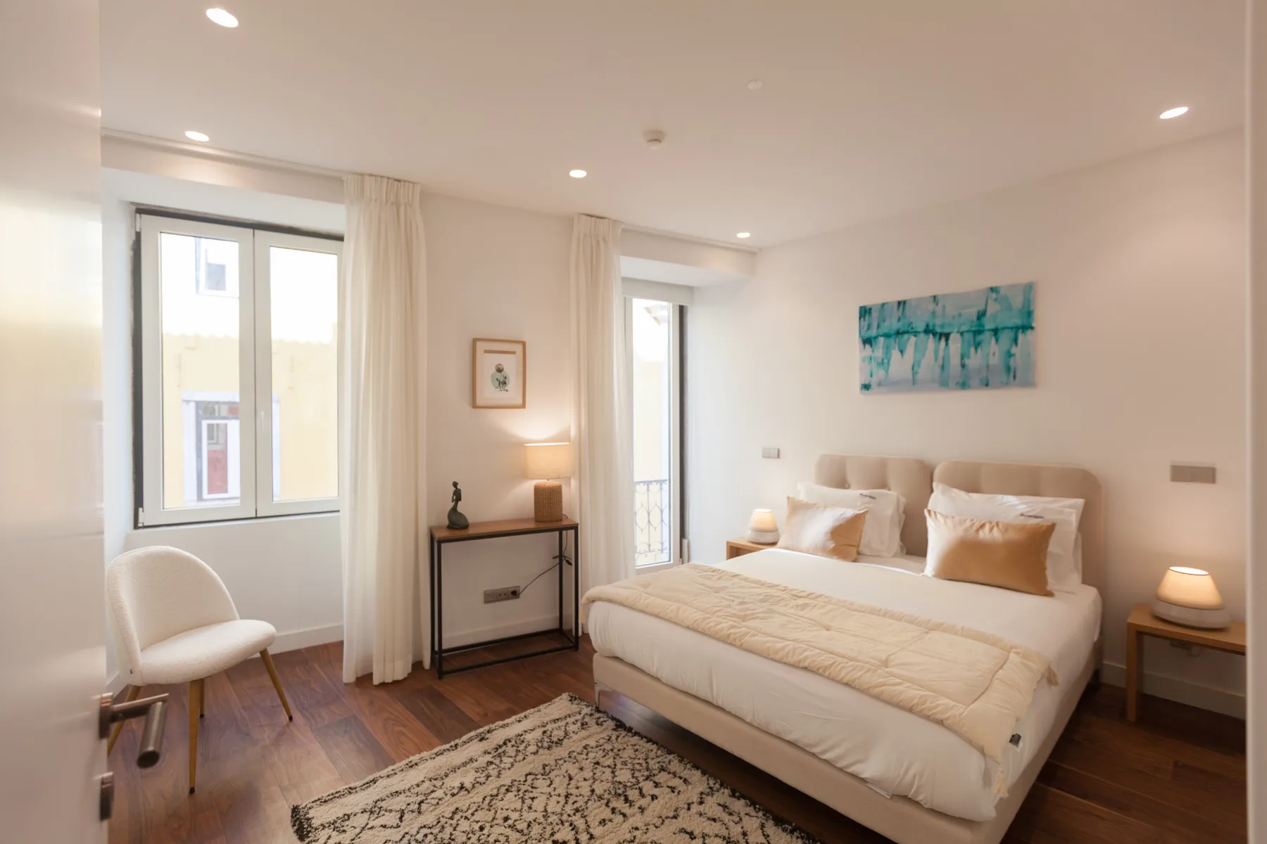 Un dormitorio luminoso con cama doble, mesillas y ventanas altas.