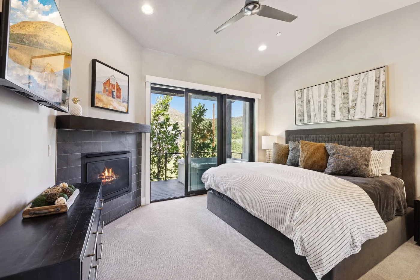 A bright bedroom with a large bed, a fireplace, and glass doors opening to a balcony.