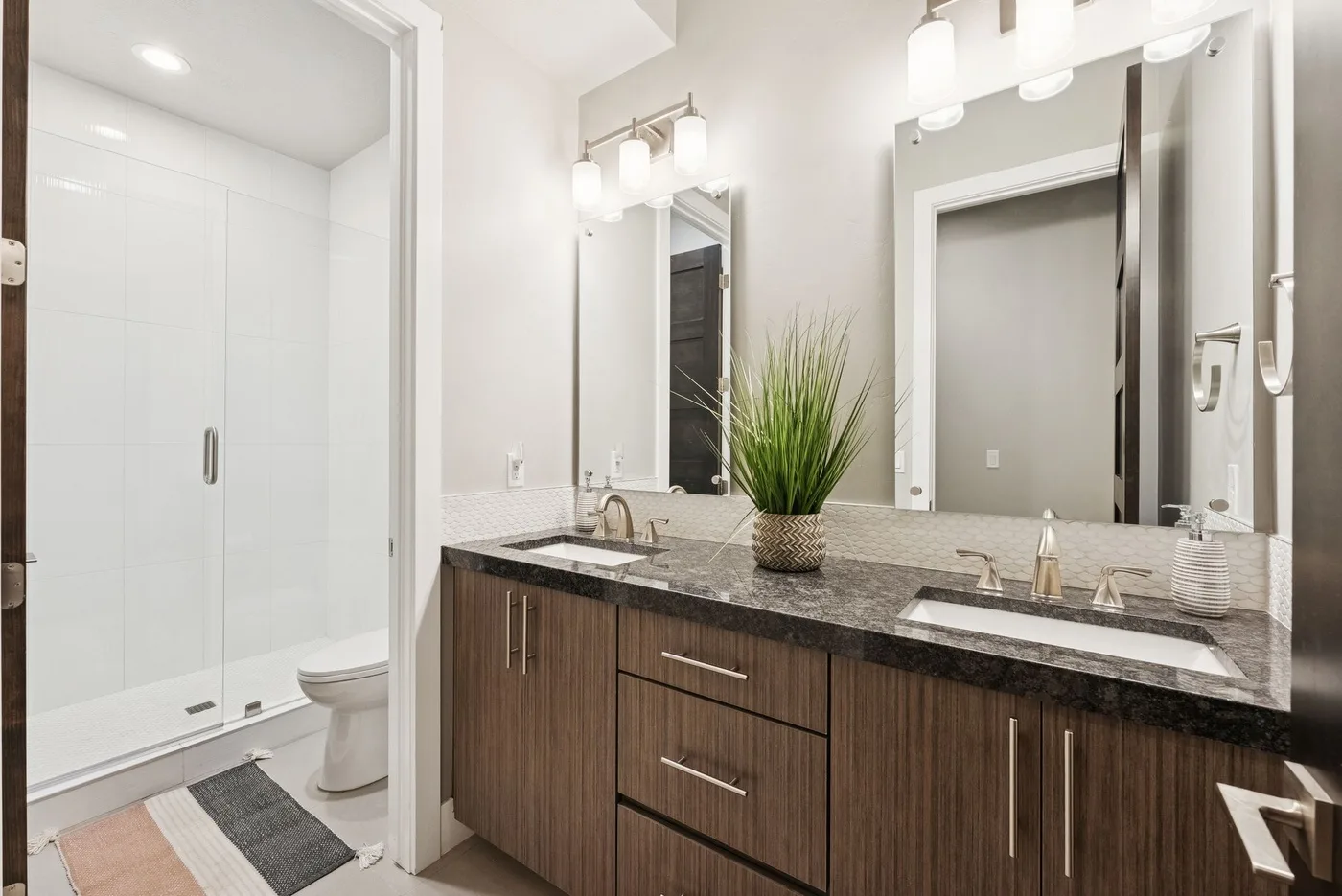A bright bathroom with a long vanity, mirrors, and a glass shower.