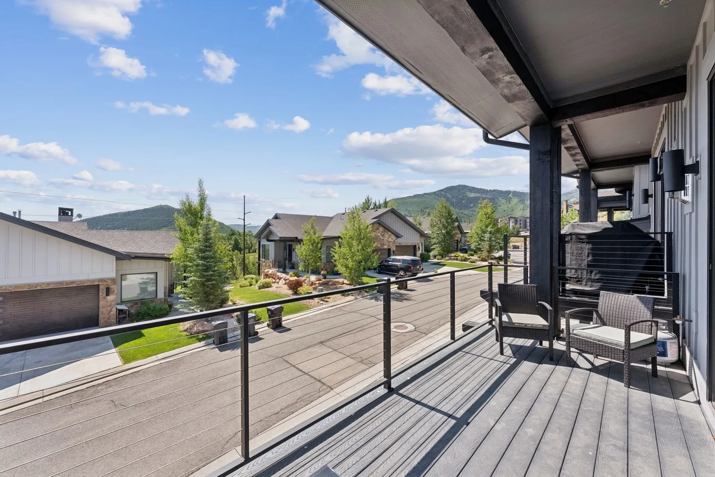 A balcony with outdoor seating overlooks a residential street and green hills.
