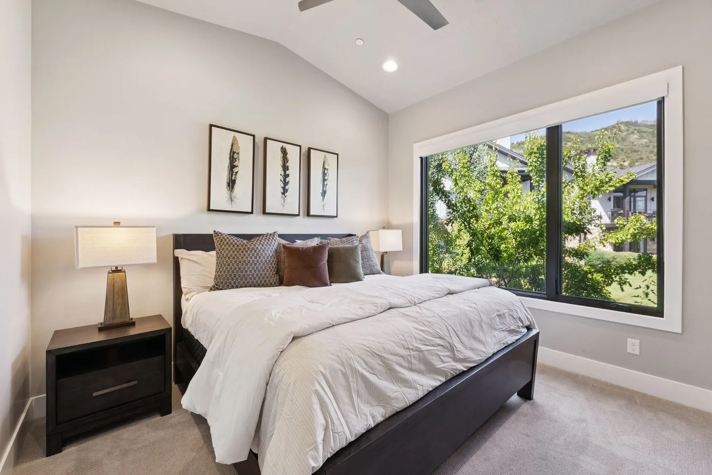 A bedroom with a neatly made bed and a large window overlooking greenery.