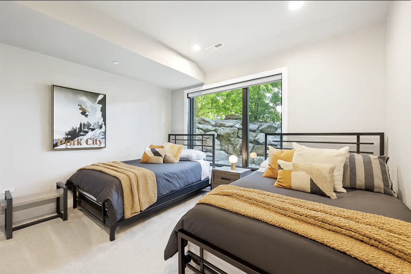 A bedroom with two beds and a large window overlooking greenery.