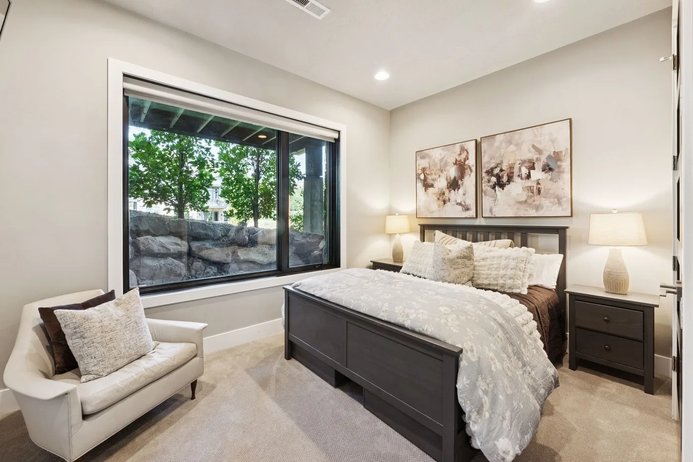 A bedroom with a bed, a cushioned chair, and a large window.