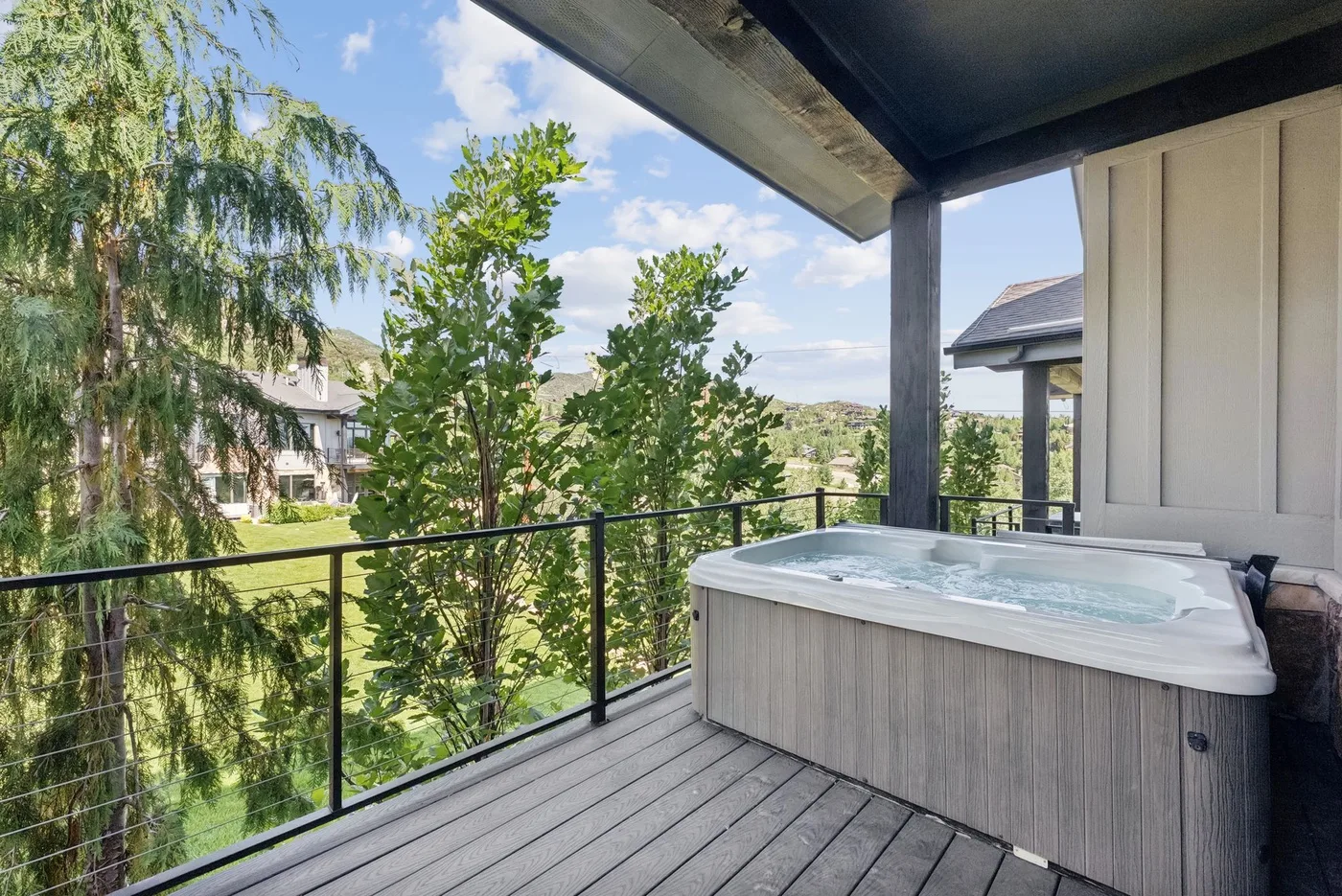 A covered outdoor deck with a hot tub overlooks trees and nearby homes.
