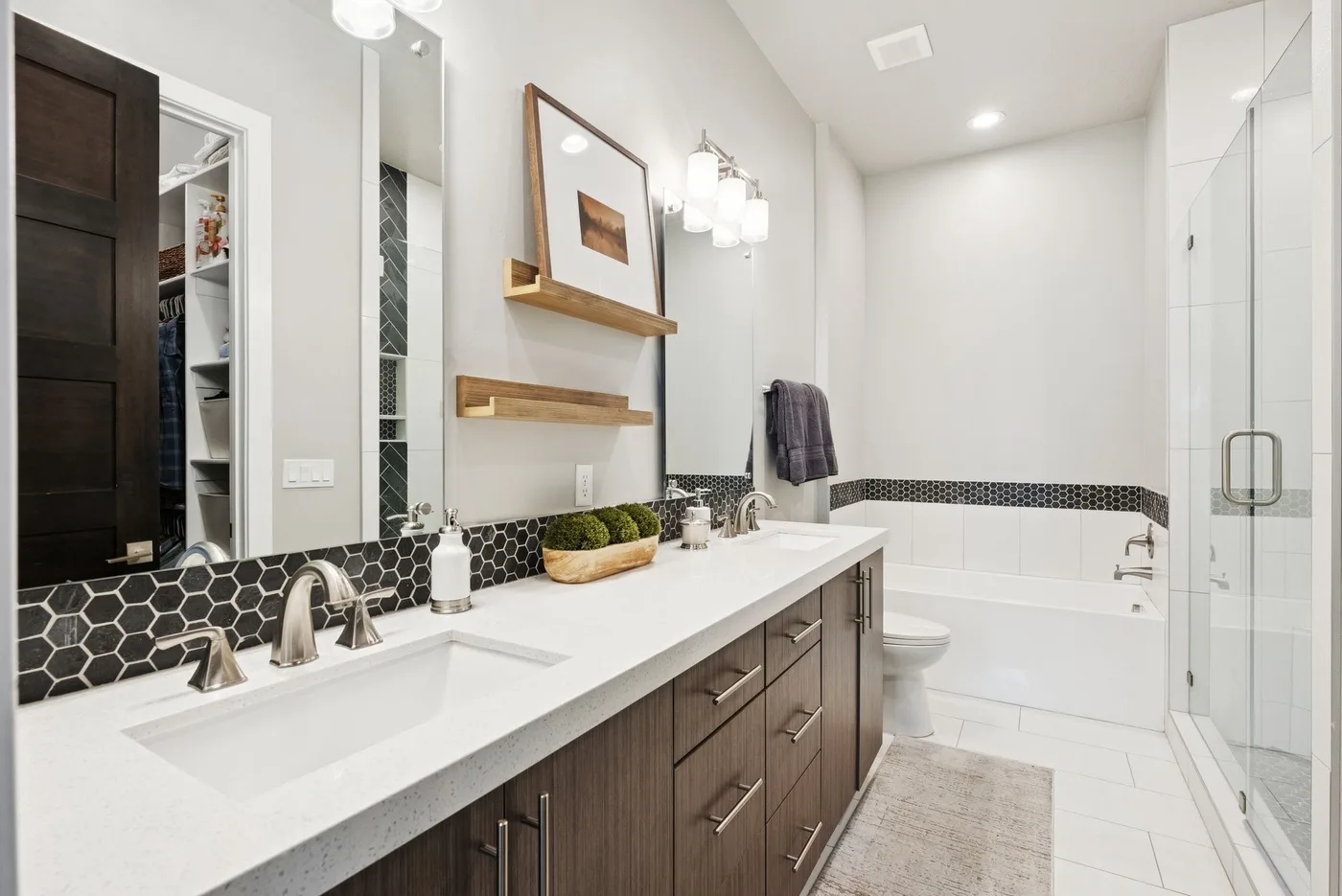 A bright bathroom with a long vanity, bathtub, and glass shower.