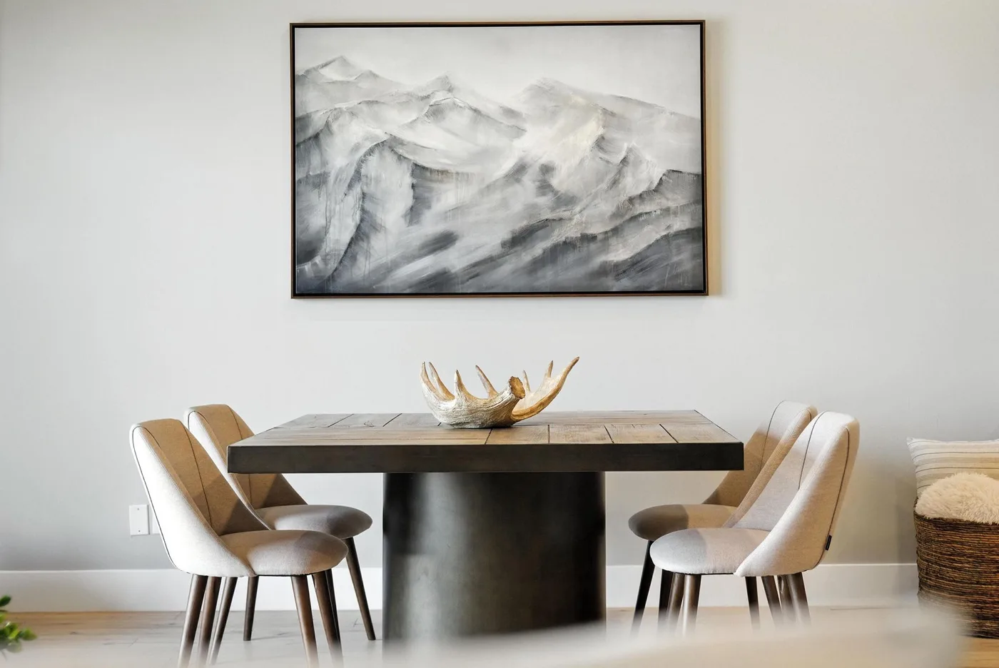 A dining area with upholstered seating, a dark pedestal table, and a framed mountain painting.