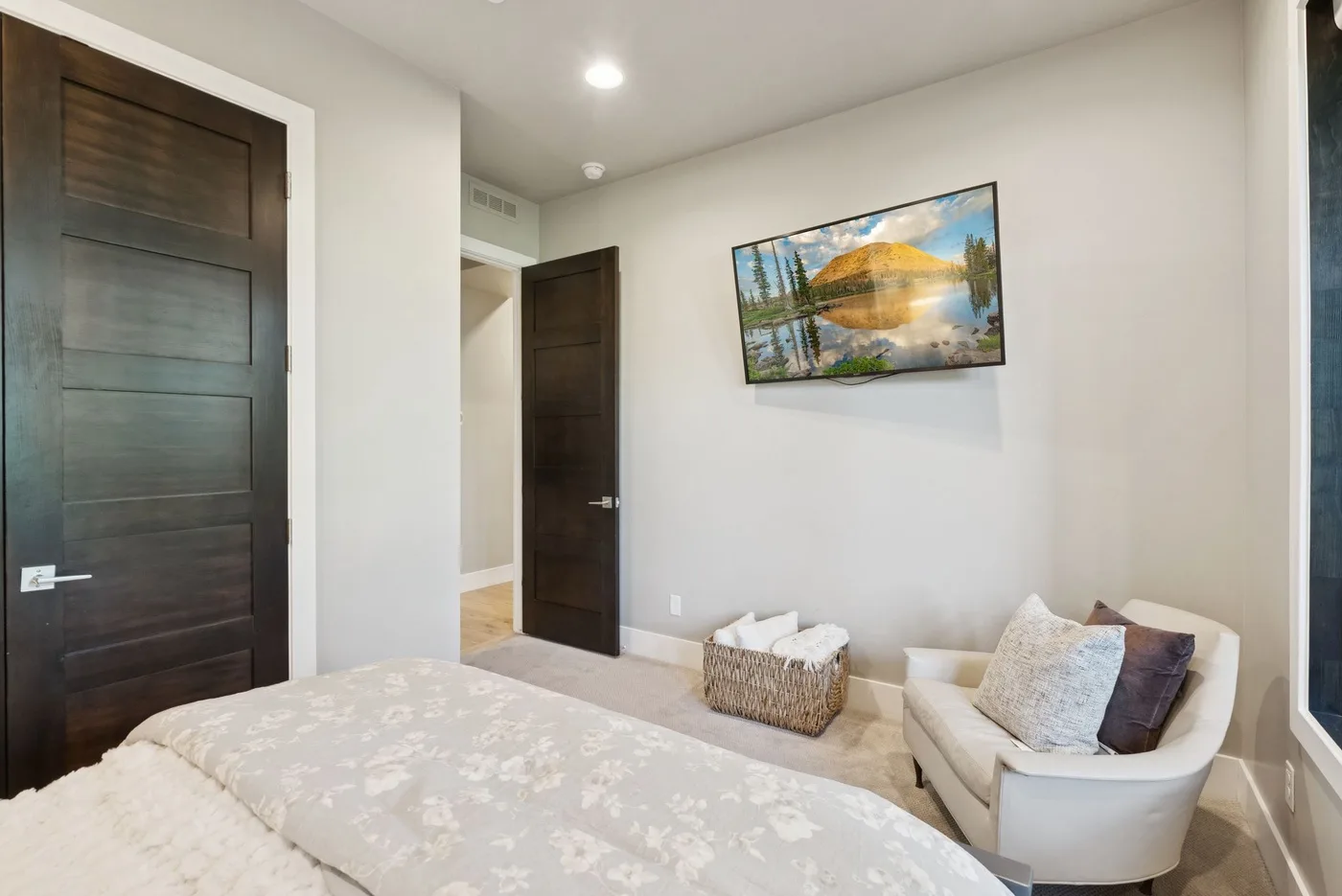 A bedroom with a bed, a cushioned chair, and a framed landscape picture.