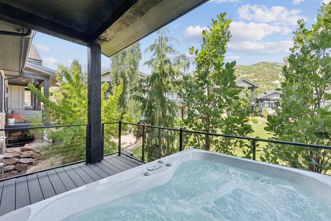 A bubbling hot tub sits on a covered outdoor deck overlooking leafy gardens.