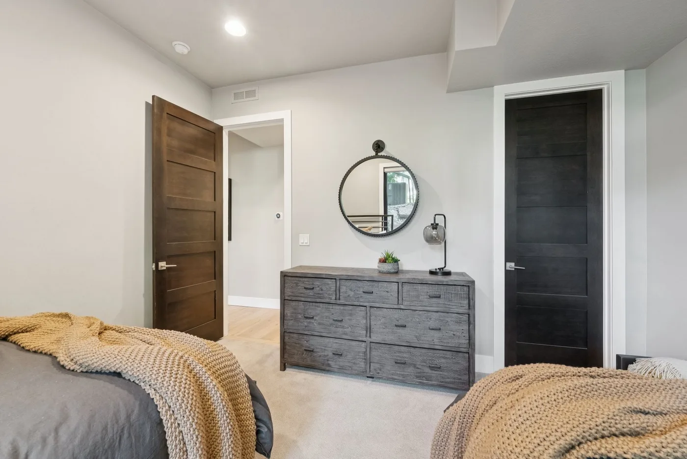 Bedroom with a dresser, round mirror, and two open doorways.