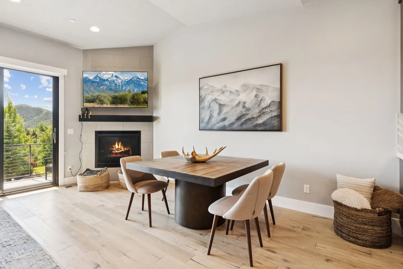 A bright dining area with a wooden table, upholstered seating, and mountain artwork.