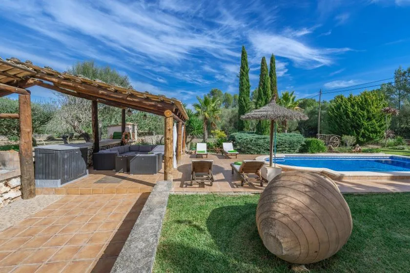 Un patio ajardinado con piscina y asientos a la sombra de una pérgola de madera.