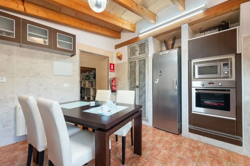 Comedor con una mesa oscura y asientos blancos junto a la cocina.