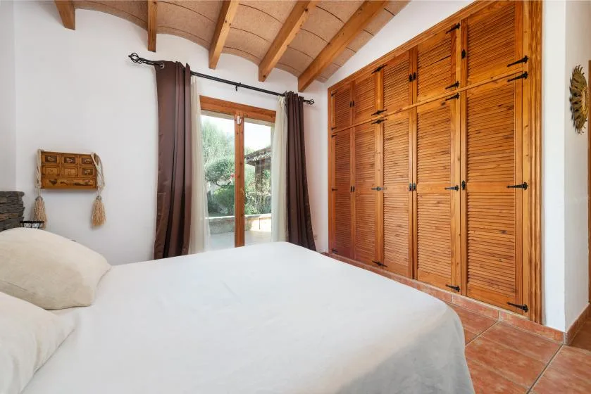 Un dormitorio con una cama junto a puertas de armario de madera con celosías y una puerta de vidrio.