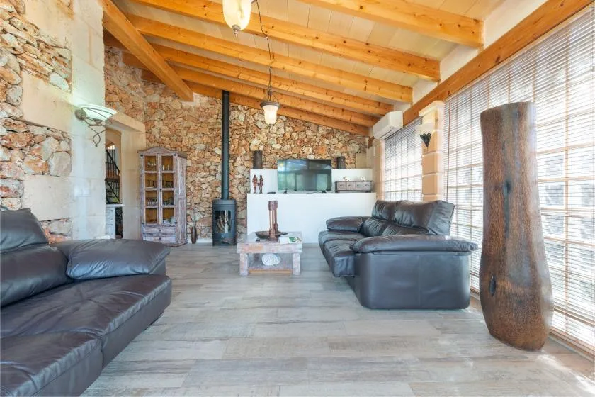 Una sala de estar con asientos oscuros, una pared de piedra y vigas de madera expuestas.