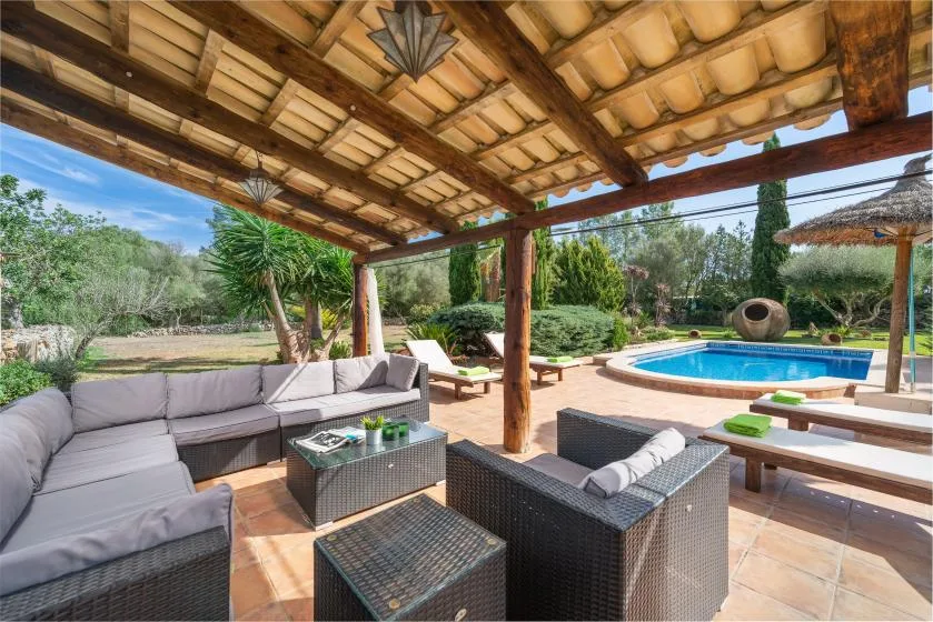 Una zona de estar exterior cubierta da a una piscina y un jardín con plantas.