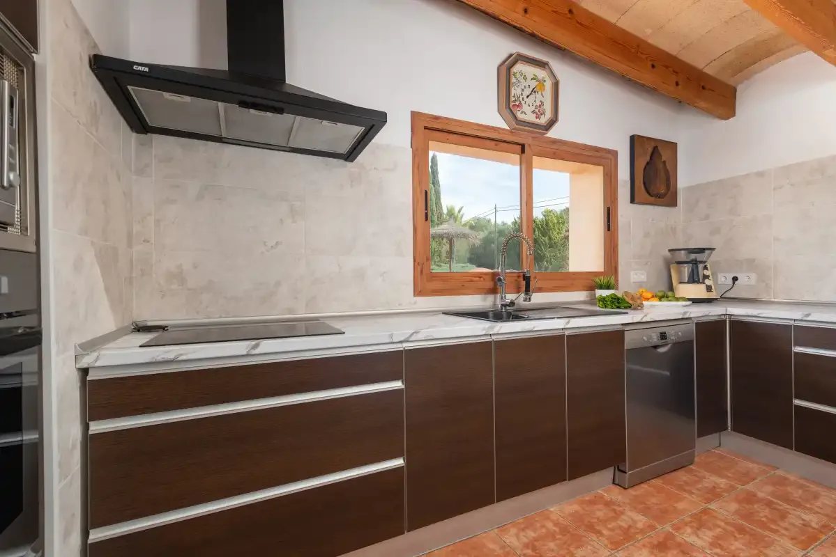 Una cocina con gabinetes oscuros, una placa de cocción y una ventana sobre el fregadero.
