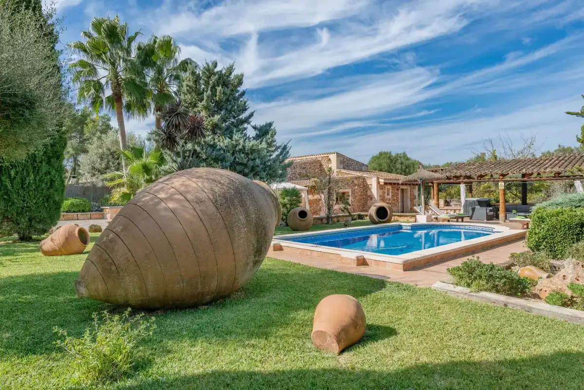 Un jardín ajardinado rodea una piscina junto a un edificio de piedra.