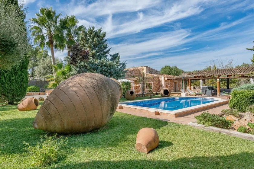 Una piscina al aire libre está junto a un jardín con césped y grandes vasijas de terracota.