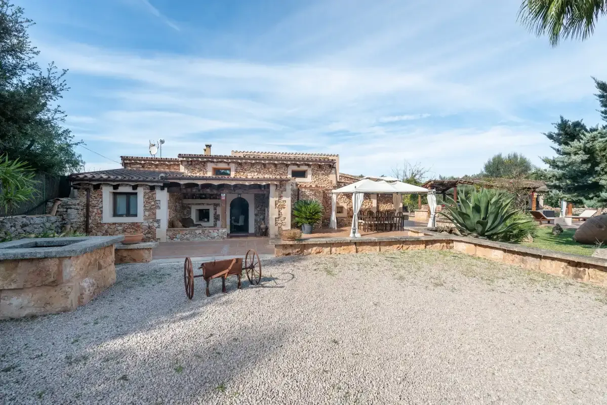 Una casa de piedra se alza junto a un patio de grava con una zona de estar cubierta.