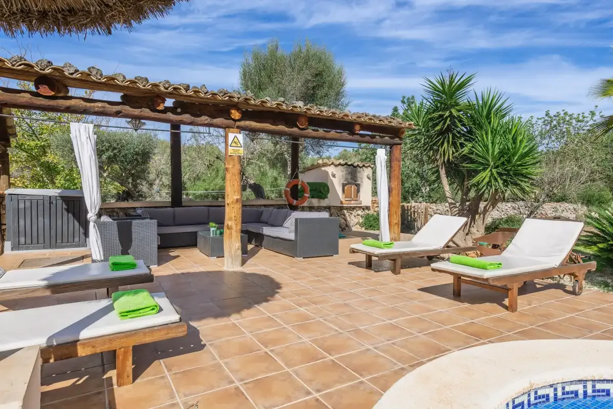Un patio exterior de baldosas tiene asientos y tumbonas junto a una piscina.