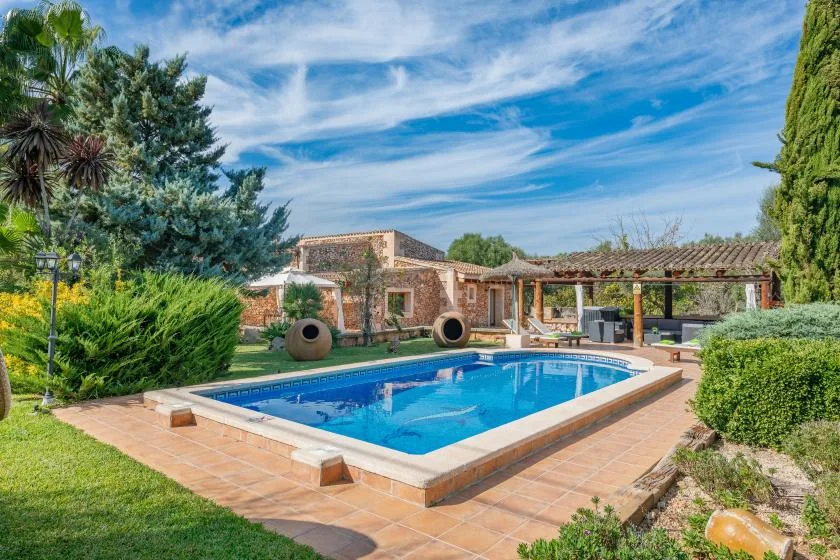 Una piscina al aire libre está junto a una casa de piedra y un patio cubierto.