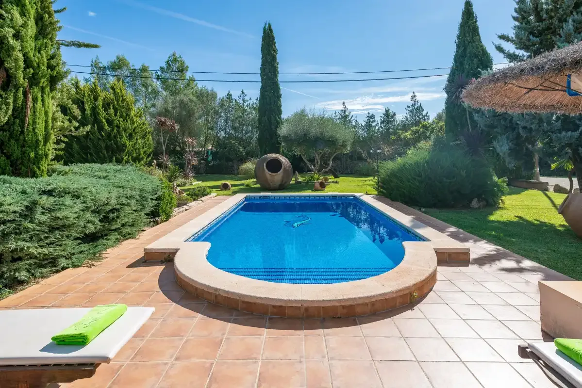 Una piscina al aire libre está rodeada de suelo embaldosado y vegetación ajardinada.
