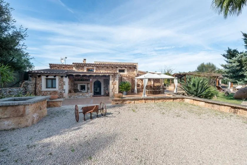 Una casa de piedra da a un patio de grava con una zona de estar a la sombra.
