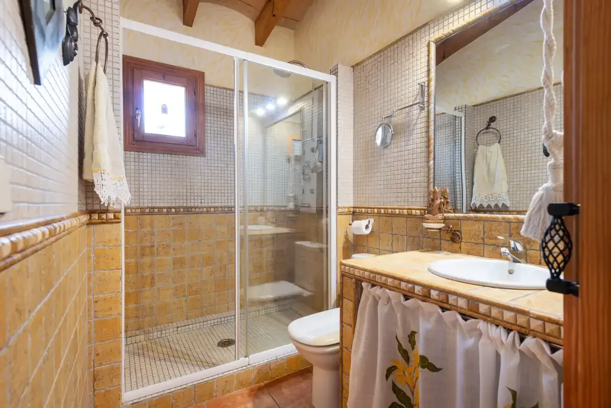 Un baño alicatado con ducha de vidrio y lavabo bajo un espejo grande.