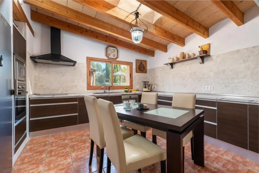Una zona de comedor en la cocina con una mesa bajo vigas de madera expuestas.